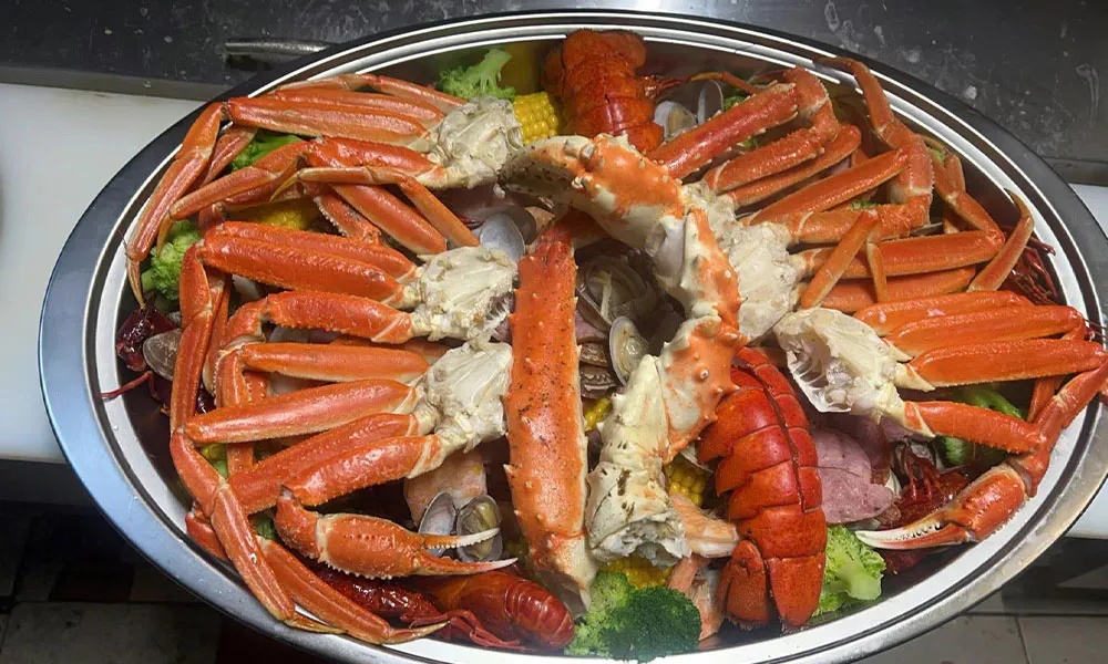 Large metal seafood boil platter piled with king crab legs, lobster tails, clams, corn and broccoli at Sushi & king seafood , a Sushi Restaurant in Commack